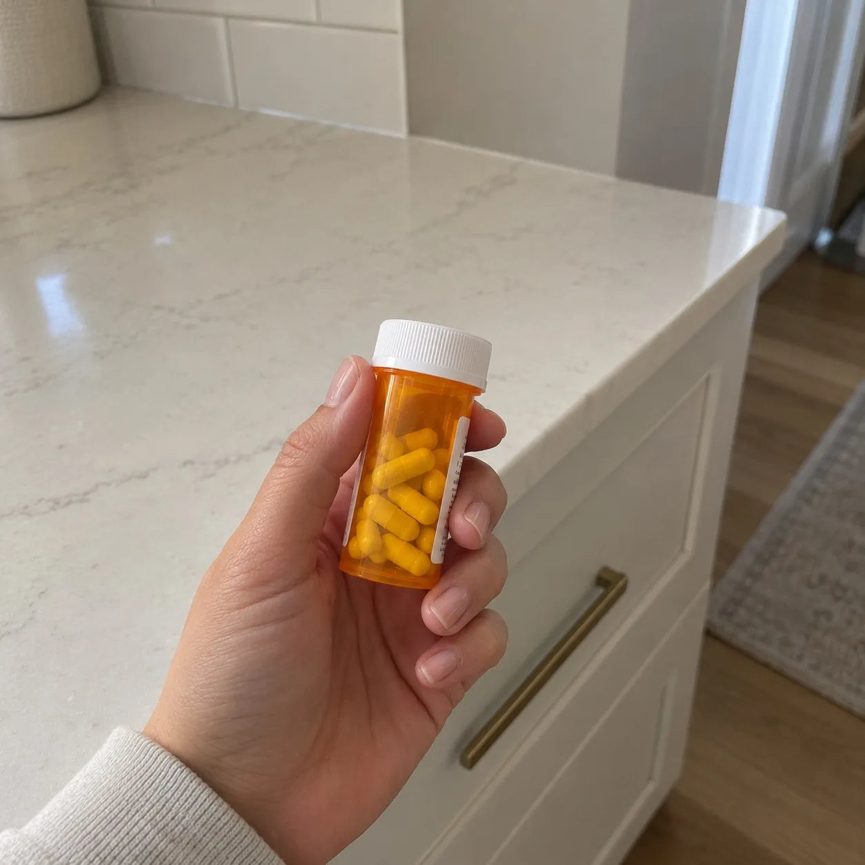 Hand holding an orange prescription pill bottle in a kitchen