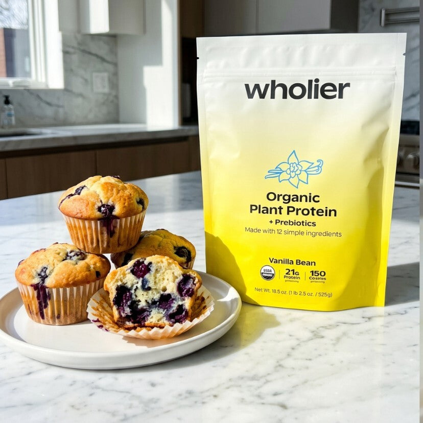 wholier Organic Plant Protein Vanilla Bean pouch beside a plate of blueberry protein muffins