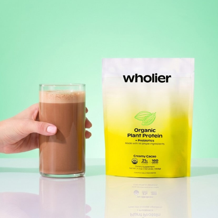 Hand holding a wholier Creamy Cacao protein shake beside the pouch