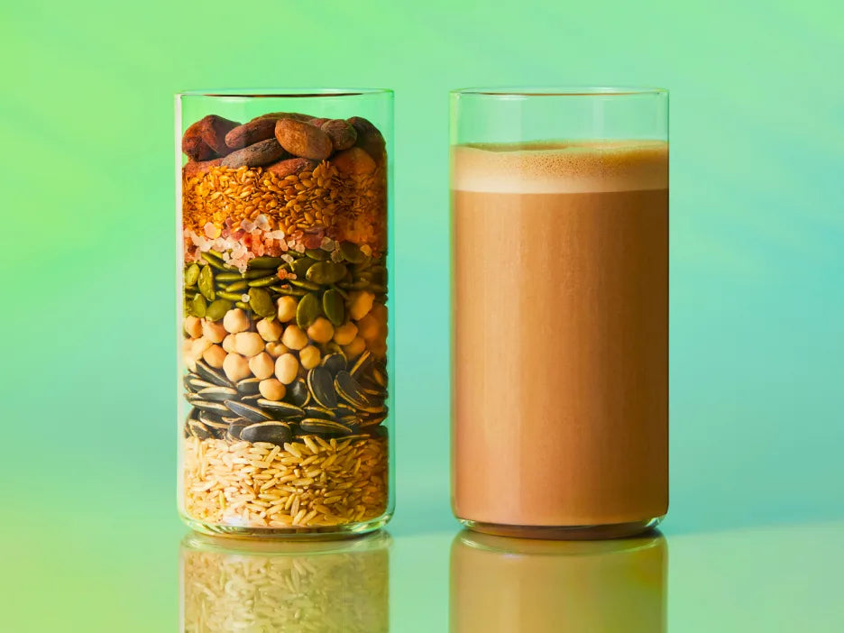 One glass layered with the raw organic plant ingredients beside a glass of the blended cacao shake