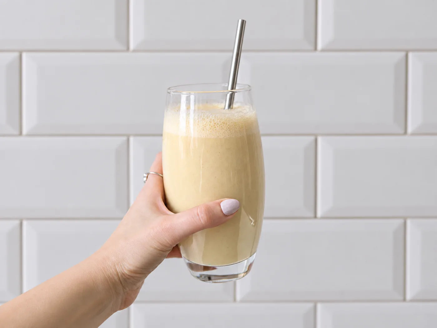 A hand holding a glass of blended Vanilla Bean shake with a metal straw