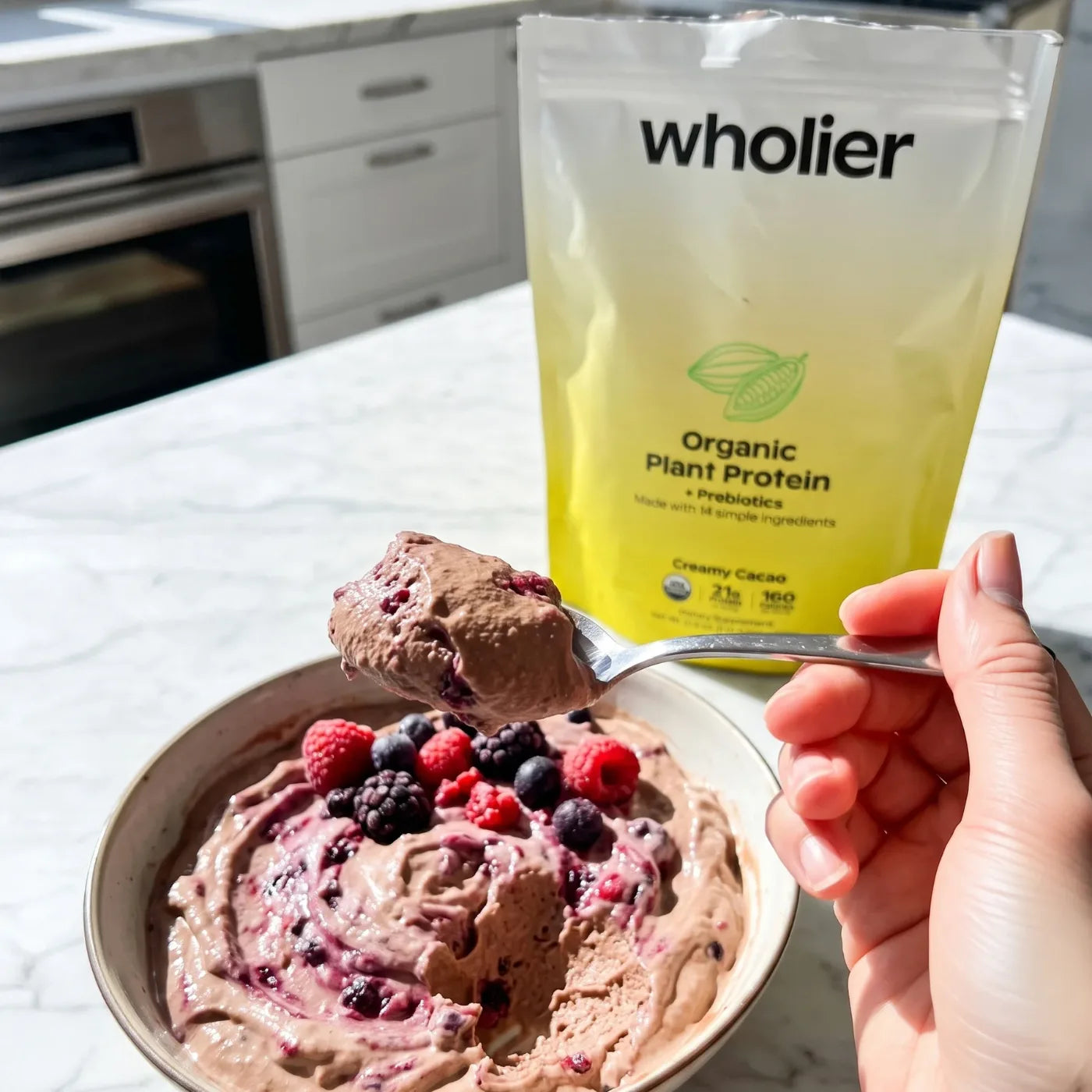 A bowl of Creamy Cacao protein pudding with berries, beside the wholier pouch