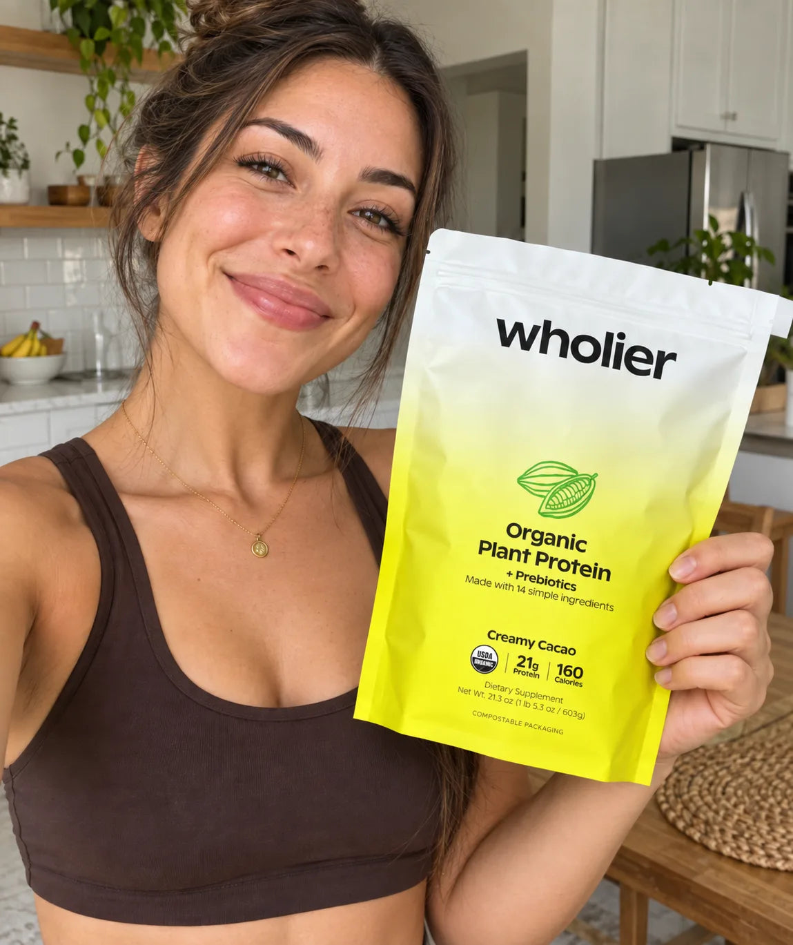 Smiling woman holding a pouch of wholier Organic Plant Protein in Creamy Cacao